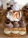 Portion cakes of meringue and cocoa butter cream in square form on a wooden stand, a piece of cake on a light wooden background.