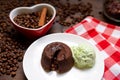 A portion of chocolate fondant with a scoop of pistachio ice cream on a plate. In the background is a heart-shaped cup filled with