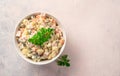 A portion of classic olivier salad with parsley on a light pink background.