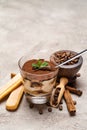 Portion of Classic tiramisu dessert in a glass cup, scoop full of coffee and cinnamon sticks on concrete background