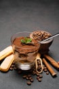 Portion of Classic tiramisu dessert in a glass cup, scoop full of coffee and cinnamon sticks on dark concrete background