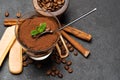 Portion of Classic tiramisu dessert in a glass cup, scoop full of coffee and cinnamon sticks on dark concrete background