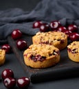 Portion crumble pie with cherries on a wooden board decorated with green mint leaves, black background