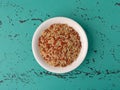 A portion of long grain brown rice and red rice in a white bowl atop a green and black tabletop