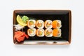 A portion of maki sushi with an assortment of Japanese side dishes in a rectangular ceramic plate on a white plate. Royalty Free Stock Photo