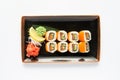 A portion of maki sushi with an assortment of Japanese side dishes in a rectangular ceramic plate on a white plate. Royalty Free Stock Photo