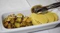 Portion potatoes of two types on one plate. Rectangular white plate with iron tongs for serving rustic potatoes with Royalty Free Stock Photo