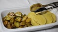 Portion potatoes of two types on one plate. Rectangular white plate with iron tongs for serving rustic potatoes with Royalty Free Stock Photo