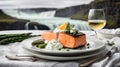 portion of smoked salmon steak and asparagus in a white plate on a white tablecloth in front of Icelandic waterfalls