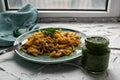 Portion of spaghetti pasta like noodles with fried vegetables on a modern plate in turquoise color, with green sauce in a jar, the Royalty Free Stock Photo