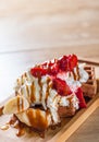 Portion of Viennese waffle with cream, strawberry, banana, caramel and ice cream on wooden table