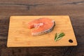 Portioned salmon steak on a wooden cutting board with a sprig of rosemary over a wooden background.