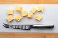 Portions cubes, dice of Emmental Swiss cheese. On white marble board and knife to cut cheese