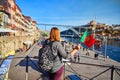 Porto, Portugal - 09 of December, 2018: Young woman traveler standing back with portuguese flag, enjoying beautiful cityscape