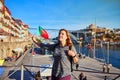 Porto, Portugal - 09 of December, 2018: Young woman traveler standing back with portuguese flag, enjoying beautiful cityscape