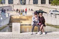 PORTO, PORTUGAL - MARCH 26, 2018: Couple sitting on a bench, smiling girl and Guy with browsing internet on smartphone