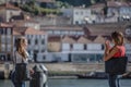 View of two girls taking photos with mobile phone, near the river with downtown on background