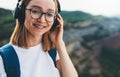 Portpait smiling young woman traveler with backpack and hipster glasses listening to favorite music on wireless headphones Royalty Free Stock Photo