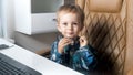 Portrai of cute smiling little boy sitting on office chair behind desk at office