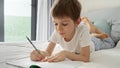Portrai of little boyworking on his homework in bed, writing in a notebook with concentration. Importance of education and child