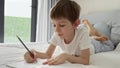 Portrai of little boyworking on his homework in bed, writing in a notebook with concentration. Importance of education.