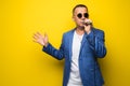 Portrai of mature middle age man in suit singing over the microphone isolated on yellow background. Singer concept.