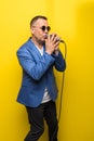 Portrai of mature middle age man in suit singing over the microphone isolated on yellow background. Singer concept.