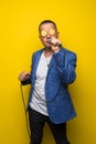 Portrai of mature middle age man in suit singing over the microphone isolated on yellow background. Singer concept.