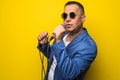 Portrai of mature middle age man in suit singing over the microphone isolated on yellow background. Singer concept.