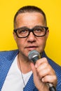 Portrai of mature middle age man in suit singing over the microphone isolated on yellow background. Singer concept.