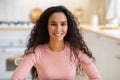 Portraif of happy young brunette woman sitting at table in kitchen