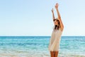 Portrair of young woman dressed in a white dress and a brown hat standing at the beach and putting hads up. Girl is engoying her Royalty Free Stock Photo