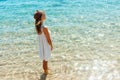 Portrair of young woman dressed in a white dress and a brown hat standing in the water and looking at the sea. Girl is engoying Royalty Free Stock Photo