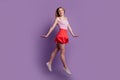 Portrait of active energetic pretty shy lady jump go wear pink top red mini skirt sneakers on purple background