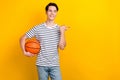 Portrait of active guy wear stylish t-shirt hold bascketball ball look directing at sale empty space isolated on yellow