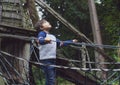 Portrait active kid climbing on rope frame at treehouse.Young boy standing alone and looking up at high forest tree near the park Royalty Free Stock Photo