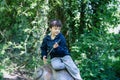 Portrait active kid sitting on a wooden statue at public park,Happy child wearing blue jacket playing outdoor in Spring forest,