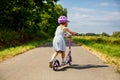 Portrait of active little preschool girl riding scooter on road in park outdoors on summer day. Seasonal child activity Royalty Free Stock Photo