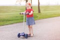 Active little toddler girl riding scooter on road in park outdoors on summer day Royalty Free Stock Photo