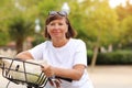 Portrait of active middle ages woman on bicycle on sunny day. Mature lady in white t shirt is riding city bike in park Royalty Free Stock Photo