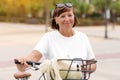 Portrait of active middle ages woman on bicycle on sunny day. Mature lady in white t shirt is riding city bike in park Royalty Free Stock Photo