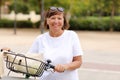 Portrait of active middle ages woman on bicycle on sunny day. Mature lady in white t shirt is riding city bike in park Royalty Free Stock Photo