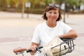 Portrait of active middle ages woman on bicycle on sunny day. Mature lady in white t shirt is riding city bike in park Royalty Free Stock Photo