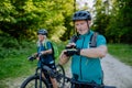 Portrait of active senior couple riding bicycles at summer park, looking at sports smartwatch, checking their Royalty Free Stock Photo