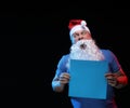 Portrait actor male in cap and beard of Santa Claus with a sheet of paper for notes in the hands