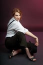 Portrait of actress with white shirt and stripped pants sits on the floor.