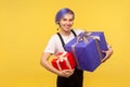 Portrait of admired joyful hipster girl holding two gifts, big and small holiday present boxes. yellow background, studio shot Royalty Free Stock Photo