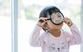 Portrait adorable Asian little girl holding magnifying glass to investigate, smiling with happiness, playing alone with copy space Royalty Free Stock Photo