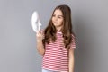 Aentive little girl in striped T-shirt holding in hands and looking at white mask with interest. Royalty Free Stock Photo