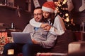 Portrait of an adorable couple - charming woman in Santa hat hugging her man and using a laptop. Royalty Free Stock Photo